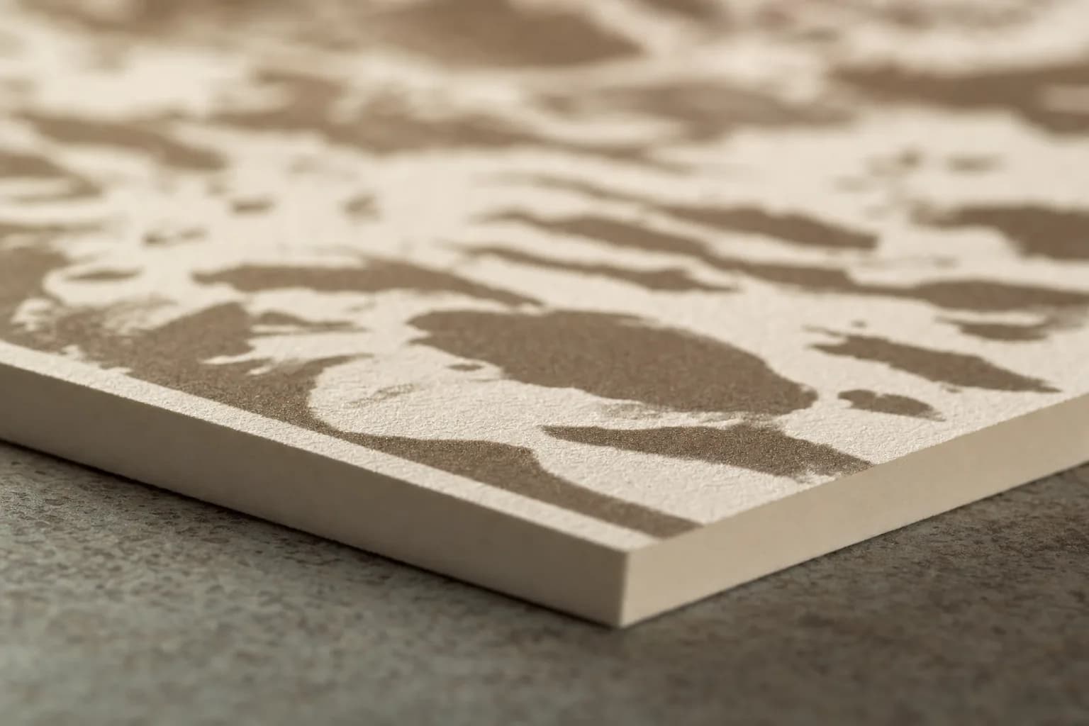 Bone-coloured cotton art paper at a shallow angle, the clean cut edge sharp in the foreground and the printed ink relief falling out of focus behind it.