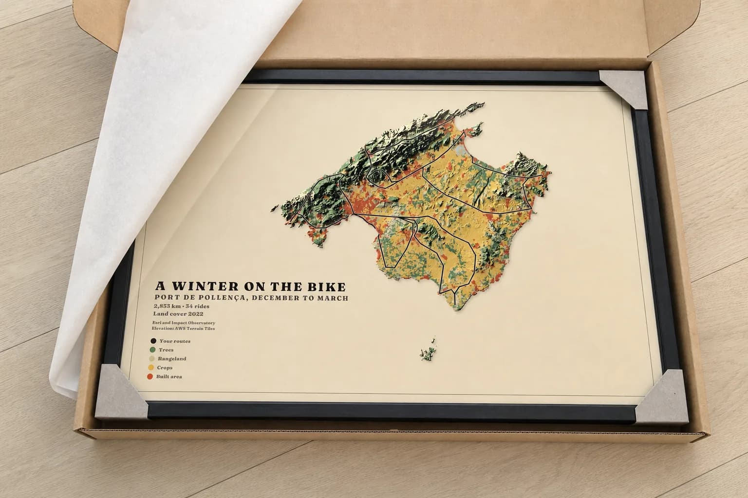 A framed map of Mallorca lying in its opened shipping box, corners held by cardboard protectors, tissue folded back.
